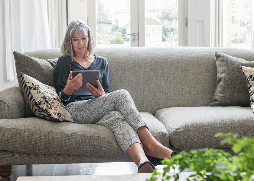 Mature woman sitting on couch with tablet